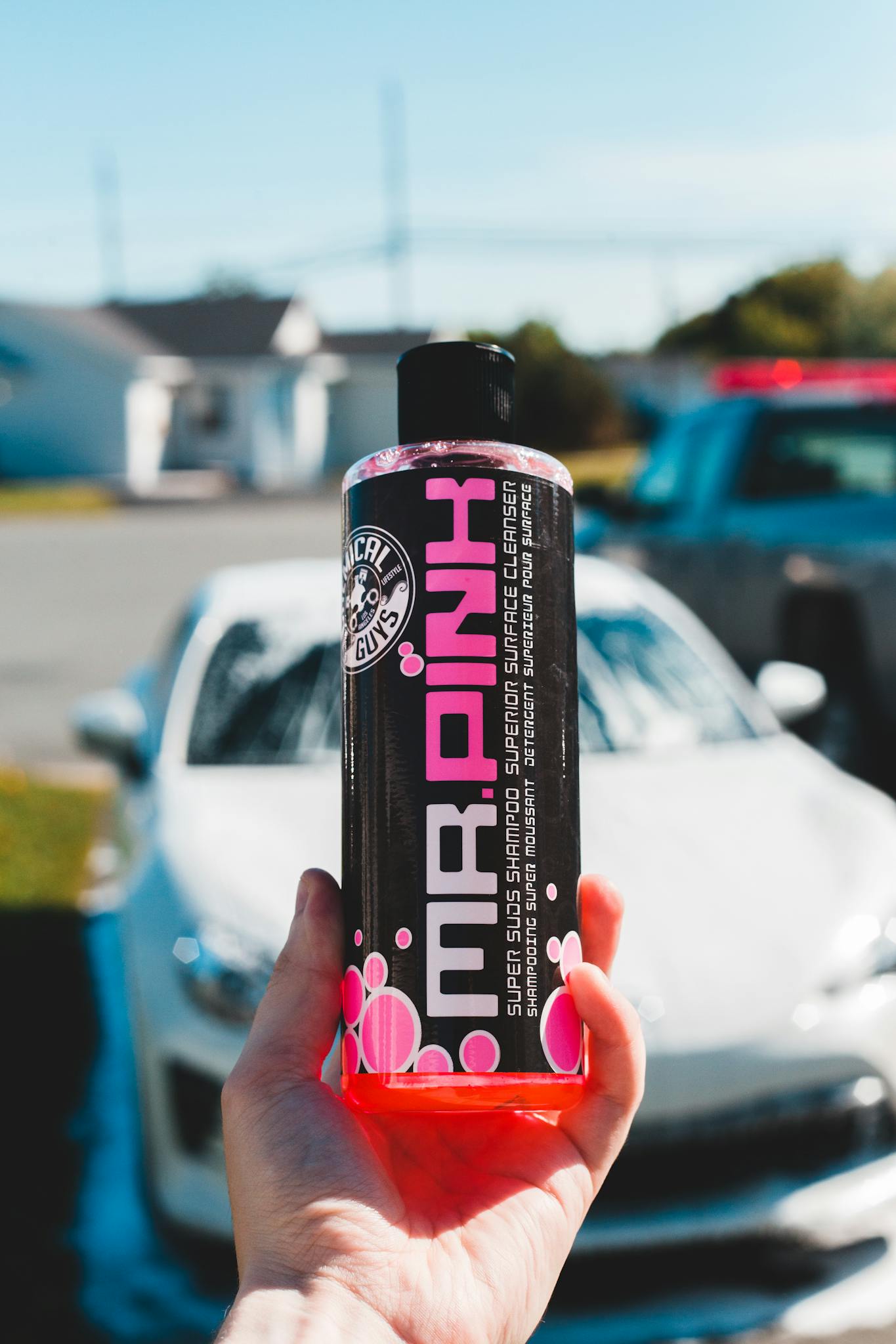 Soft focus of faceless person demonstrating bottle of car wash soap while standing in front of wet automobile on blurred background